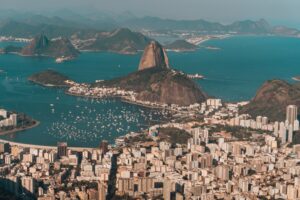 Foto aérea do rio de janeiro em um dia ensolorado, apresentando o mar, o pão-de-açúcar, a cidade e alguns outros morros.